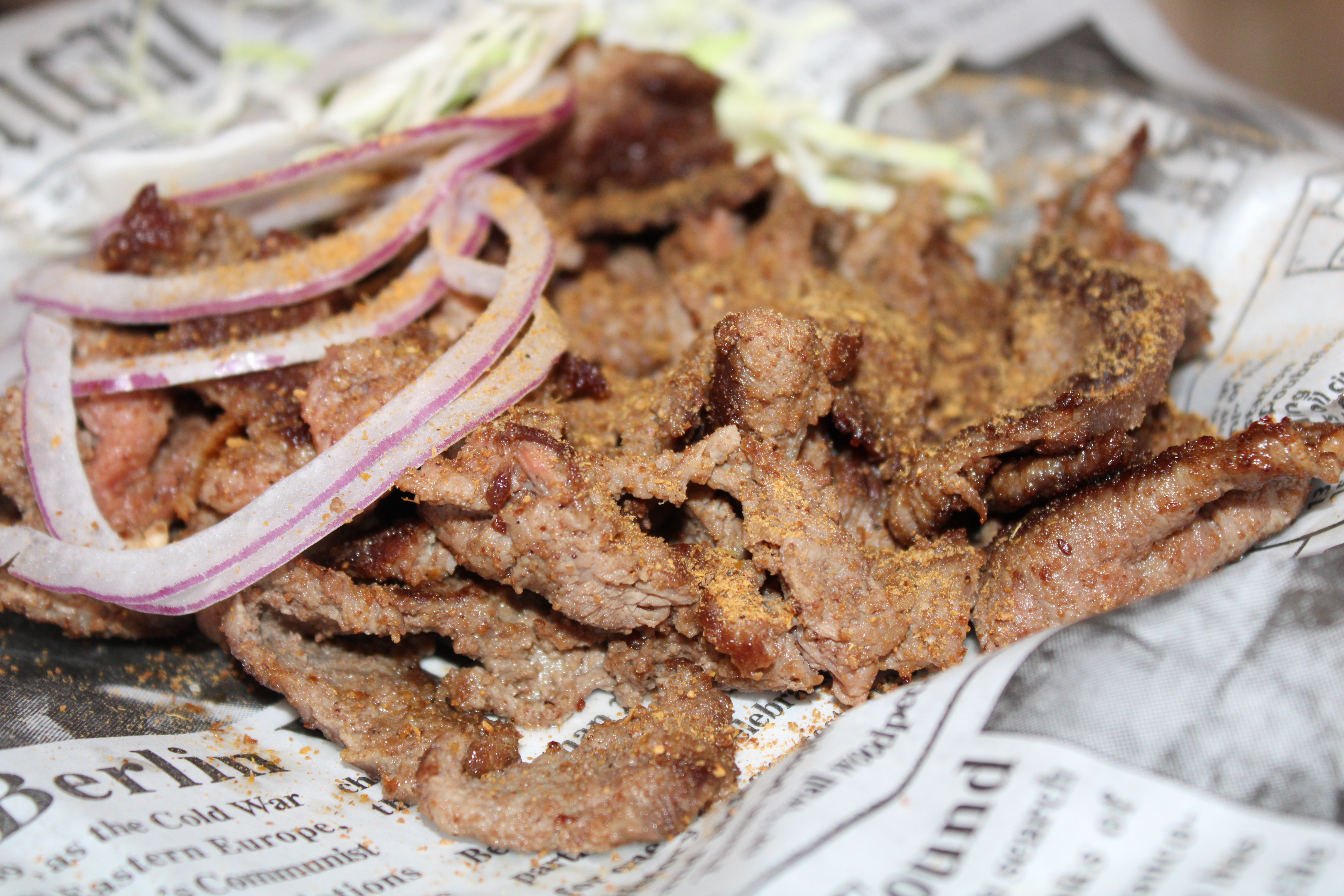 Spice-coated beef suya slices with red onion and salad garnish
